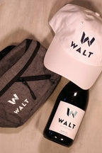 Image featuring the WALT New Era baseball cap, walt cross body bag and a bottle of WALT Blue Jay Pinot Noir.